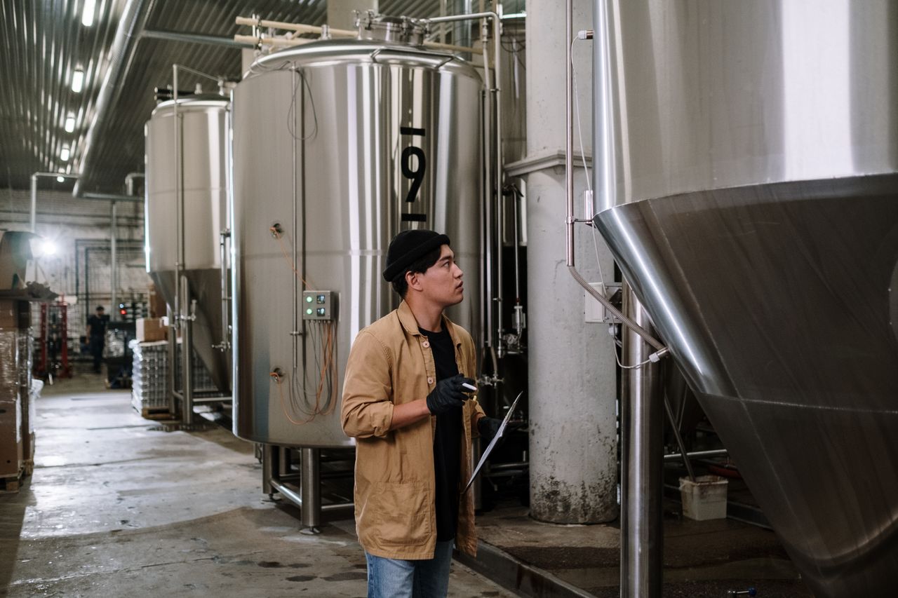 Mastering the First Impression: Your intriguing post title goes here Asian man inspecting stainless steel tanks in a brewery, showcasing modern industrial processes.